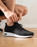 pessoa amarrando tenis preto com solado branco